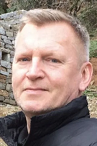 Portræt af en midaldrende mand med kort lyst hår og sort jakke.