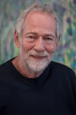 Portræt af en smilende ældre mand med gråt hår og hvidt skæg.