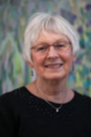 Portræt af en smilende kvinde med kort hvidt hår, briller og sort top.