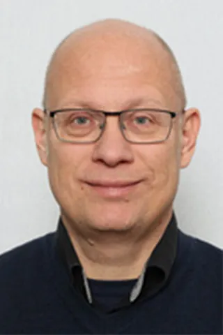 Portræt af en skaldet mand med briller og mørkeblå sweater.