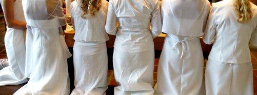 Fem konfirmander knælende ved alteret, set bagfra, i hvide kåber.