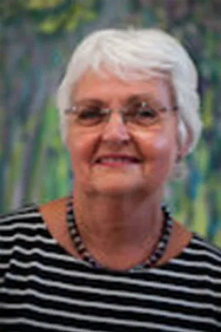 Portræt af en smilende kvinde med kort hvidt hår, briller og stribet bluse.