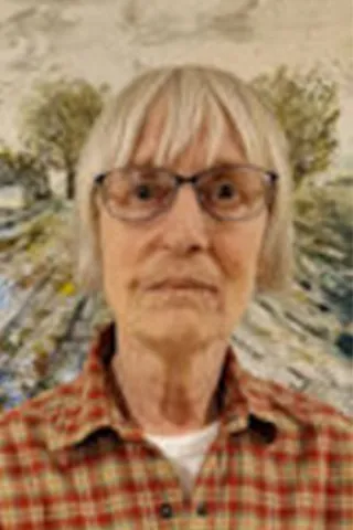 Portræt af en ældre kvinde med kort lyst hår, briller og ternet skjorte.