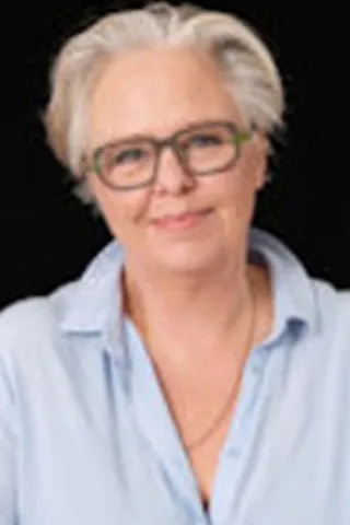 Portræt af en kvinde med kort gråt hår, briller og blå skjorte.